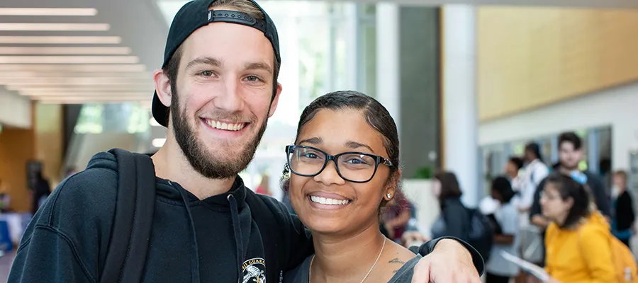 A smiling male Wake Tech student puts his arm around the shoulder of a smiling female student