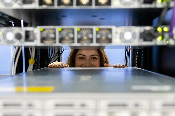 A female Wake Tech student peeks through an array of computer servers.