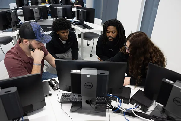 A group of Wake Tech students gather around a computer to collaborate on a Cloud Infrastructure assignment.