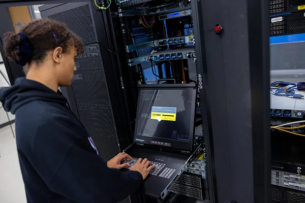 A female Wake Tech student types commands into a computer server.