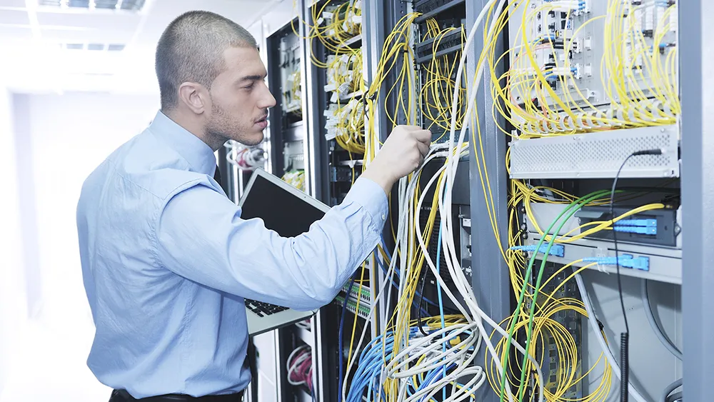 A man checks the cable connections in a computer server room.