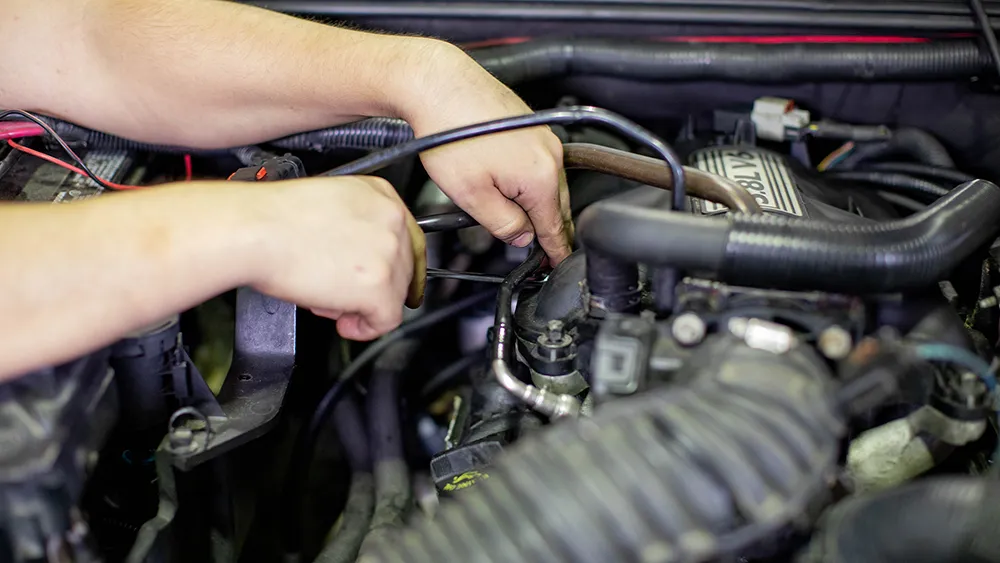 A student performs maintenance on a car engine.