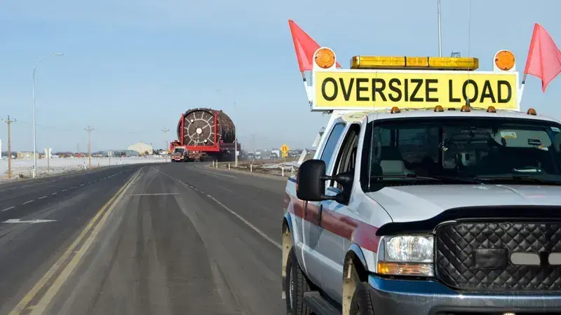 Photo of an escort vehicle guiding an oversized truck on a highway