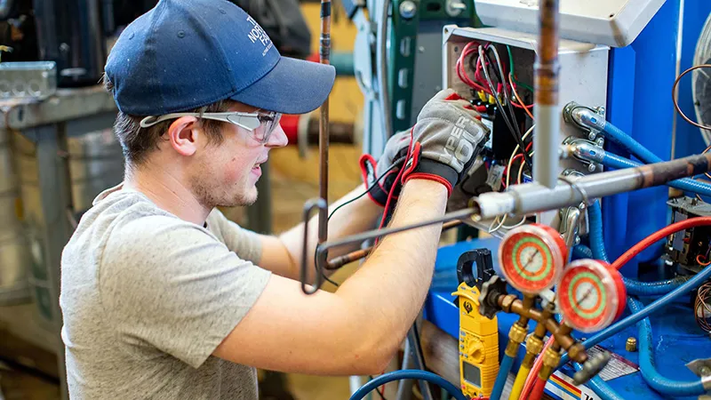 An HVAC student fixes an air conditioning unit.