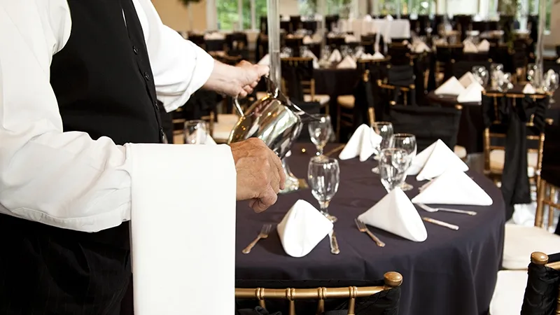 A waiter fills water glasses in a restaurant.