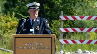 A flag flies from fire engine ladders during the groundbreaking ceremony for the Advanced Fire and Rescue Training Complex at Wake Tech East.