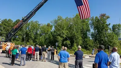 A flag flies from fire engine ladders during the groundbreaking ceremony for the Advanced Fire and Rescue Training Complex at Wake Tech East.