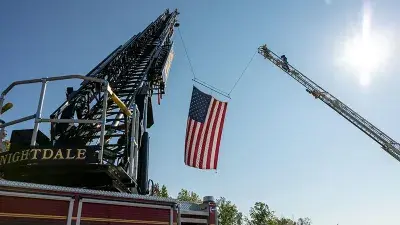 A flag flies from fire engine ladders during the groundbreaking ceremony for the Advanced Fire and Rescue Training Complex at Wake Tech East.